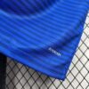 Detalle del borde inferior de la camiseta 'El Barrio' de la King League con la tecnología AEROREADY, sobre un fondo de rejilla.