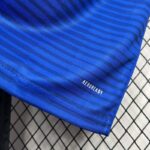 Detalle del borde inferior de la camiseta 'El Barrio' de la King League con la tecnología AEROREADY, sobre un fondo de rejilla.