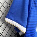 Detalle de la manga de la camiseta 'El Barrio' de la King League en color azul, con borde en blanco y dorado, mostrando la textura perforada del material para mayor transpirabilidad.